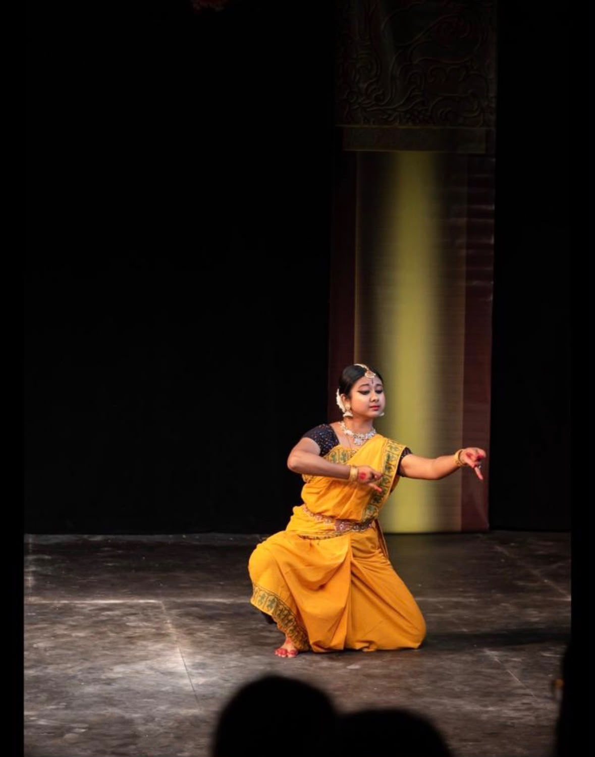 Young Bharatanatyam dancer performing expressively on stage in a yellow costume